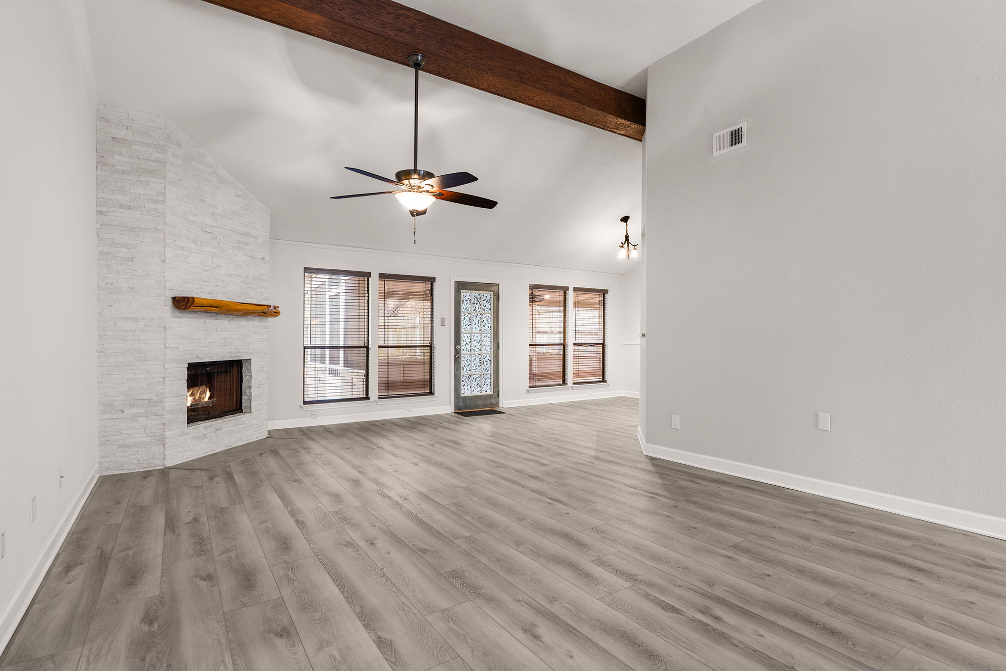 2409 Water Well Lane Austin, TX 78728 - Photo 4 of 22 Spacious interior featuring vaulted ceilings with exposed wood beams, a corner fireplace with a stacked stone facade and wood mantel, and wood-finish flooring