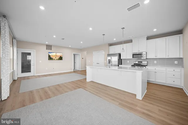 a large white kitchen with kitchen island a sink a stove a refrigerator and white cabinets with wooden floor