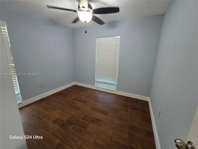an empty room with wooden floor fan and windows