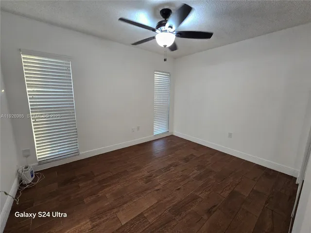 an empty room with wooden floor chandelier fan and windows