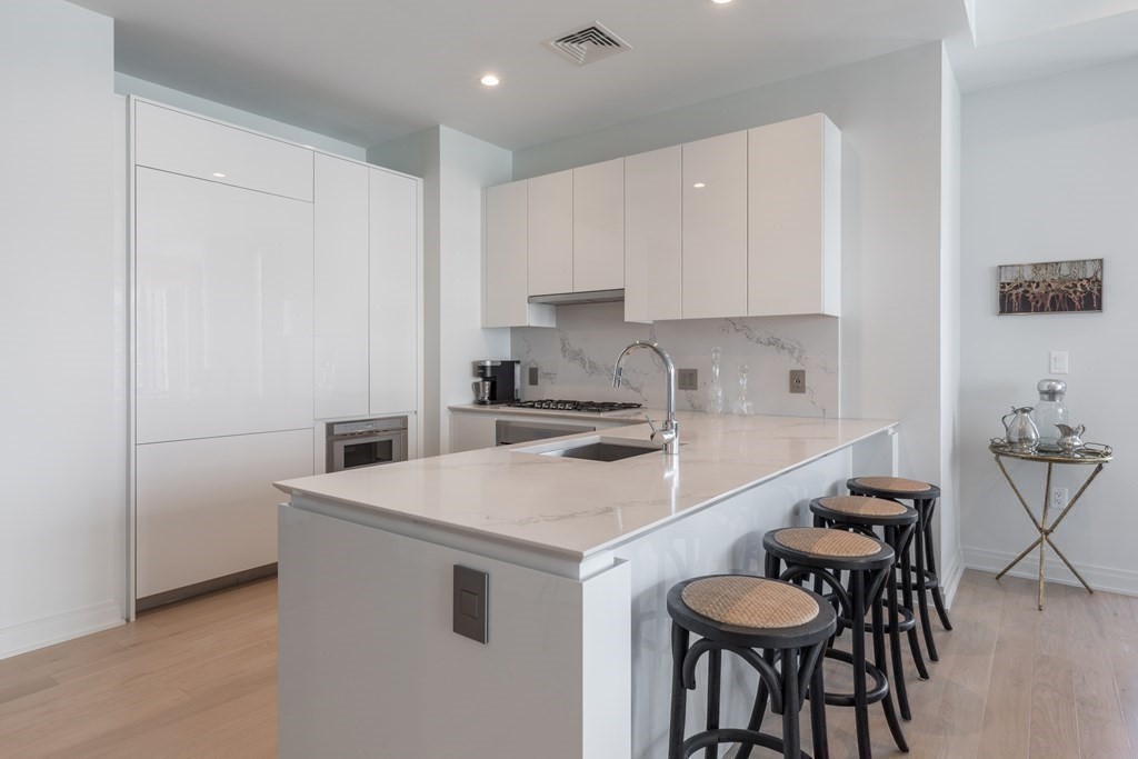 133 Seaport Boulevard, Unit 1908 Boston, MA 02210 - Photo 5 of 34 a kitchen with a sink a stove a refrigerator and white cabinets with wooden floor