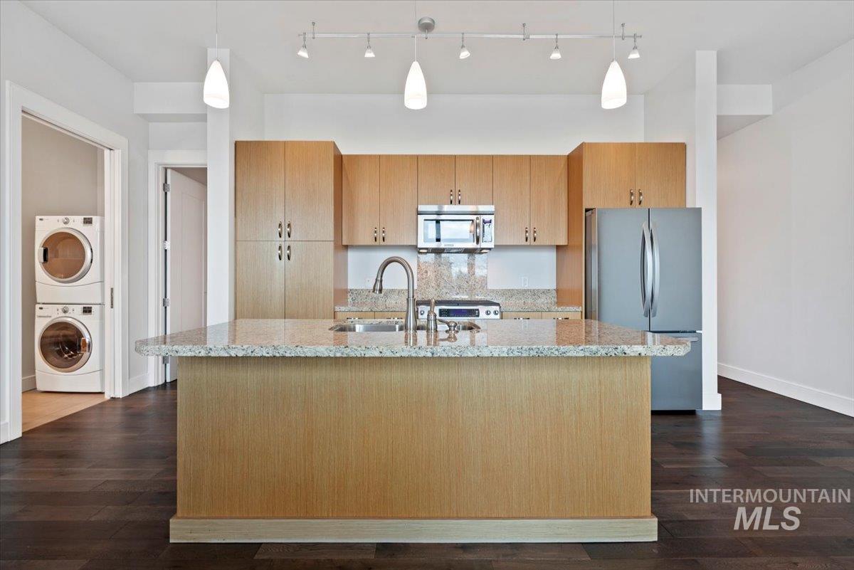 419 South 8th Street, Unit 309 Boise, ID 83702 - Photo 7 of 28 Kitchen with light stone countertops, stainless steel appliances, decorative light fixtures, a center island with sink, and dark wood-type flooring