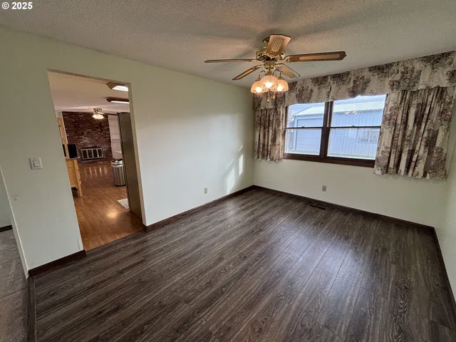 a view of an empty room with wooden floor and a ceiling fan