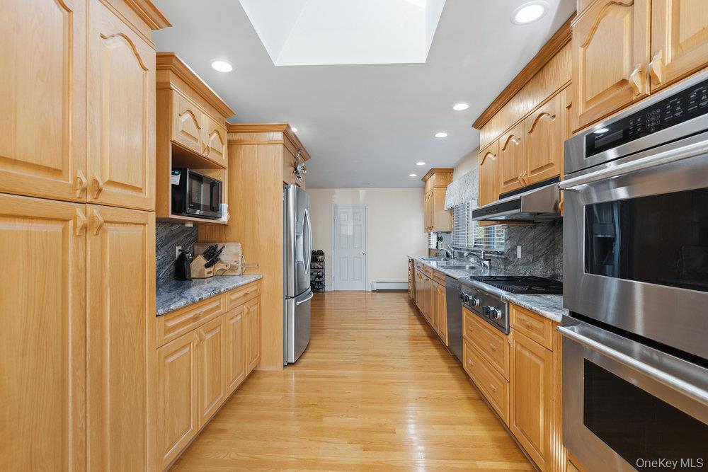 72 Lake End Road Merrick, NY 11566 - Photo 15 of 42 Kitchen with appliances with stainless steel finishes, light wood-type flooring, light stone counters, decorative backsplash, and recessed lighting