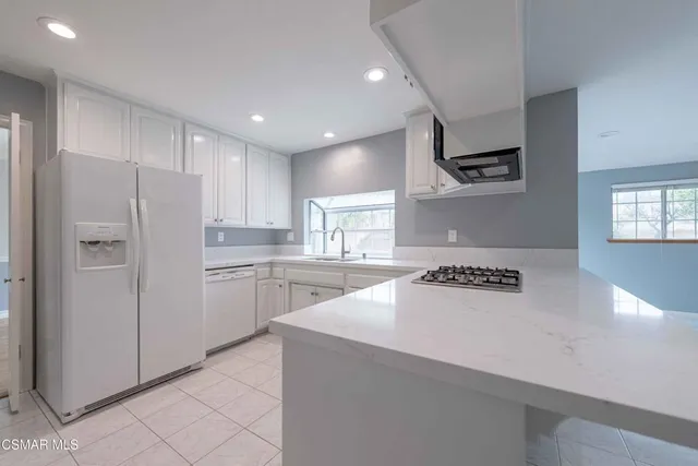 a kitchen with a refrigerator a stove top oven a sink and white cabinets