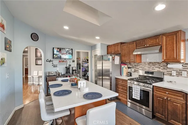 a kitchen with stainless steel appliances kitchen island granite countertop a refrigerator a stove and a dining table with wooden floor