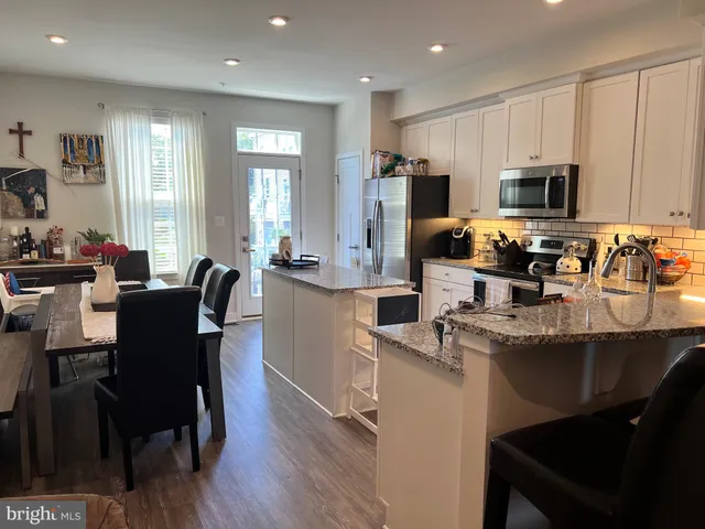 a kitchen with stainless steel appliances granite countertop a sink a stove a refrigerator a dining table and chairs