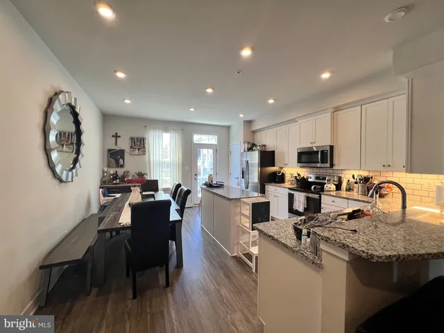 a large kitchen with kitchen island granite countertop a stove a sink a dining table and chairs with wooden floor