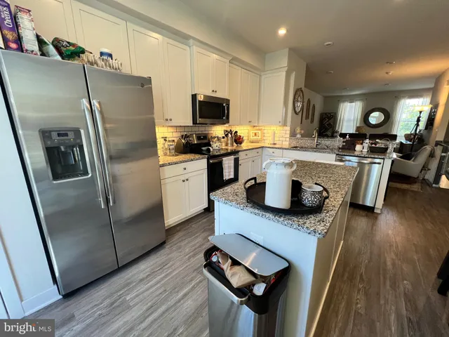 a kitchen with a refrigerator a sink dishwasher a stove and a dining table with wooden floor