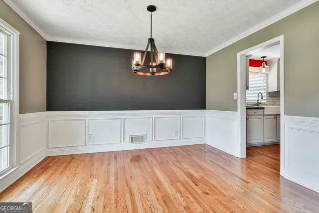 a view of an empty room with wooden floor and kitchen view