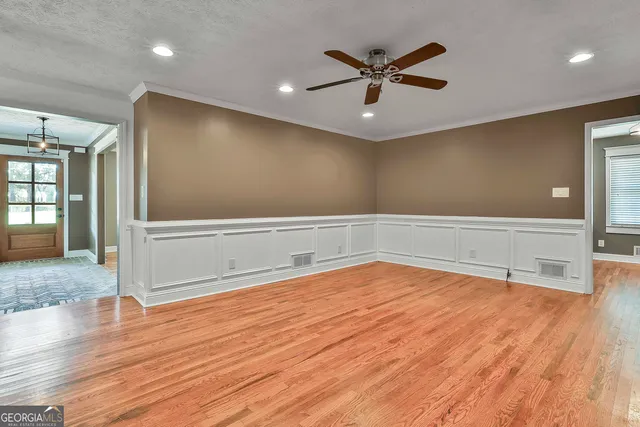 a view of an empty room with wooden floor and a ceiling fan