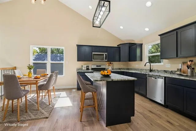 a kitchen with stainless steel appliances granite countertop a stove top oven a sink dishwasher a dining table and chairs with wooden floor