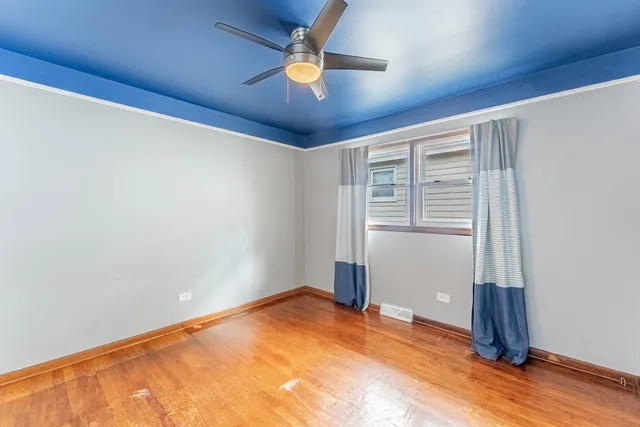 an empty room with wooden floor fan and windows