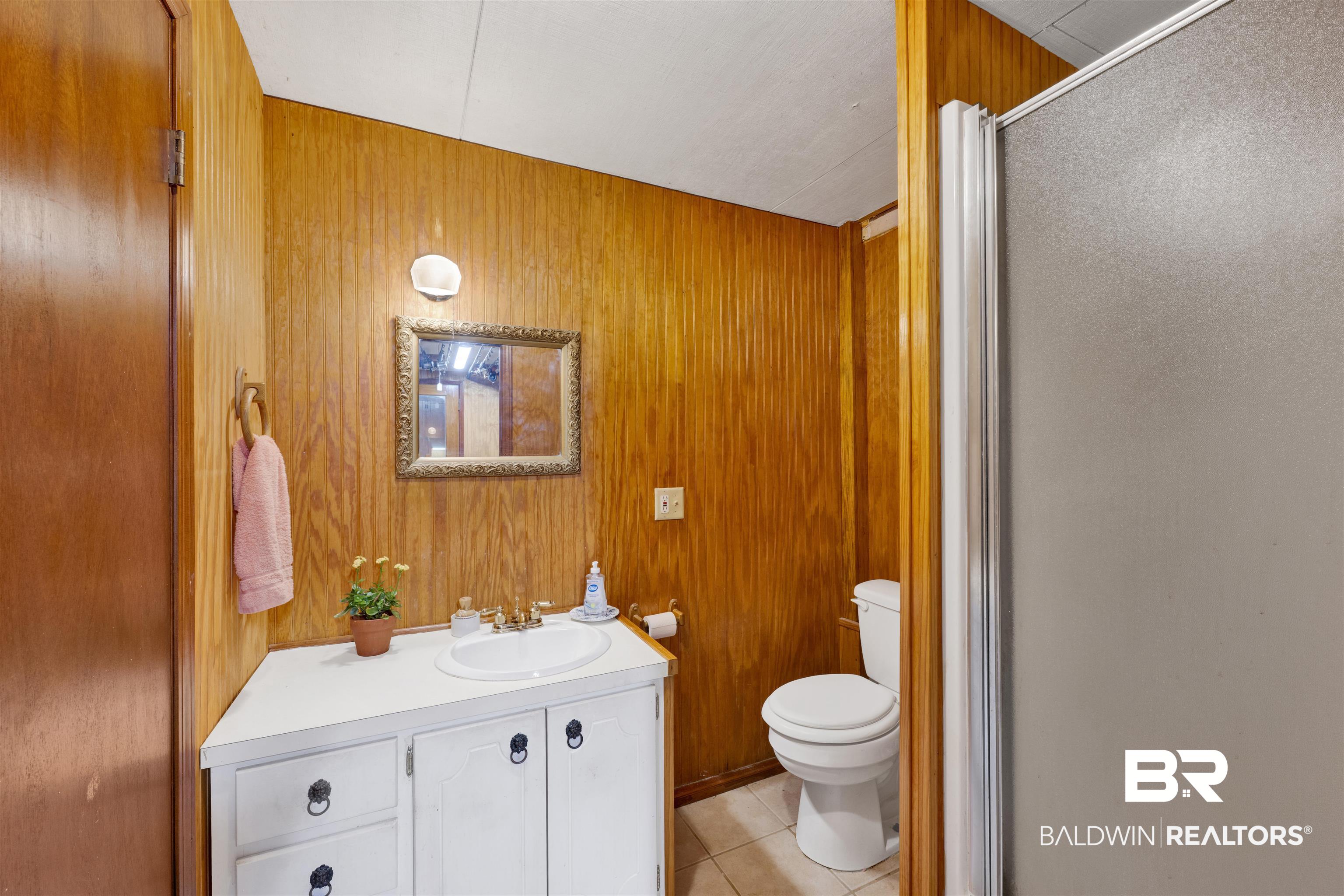 26222 Marina Road Orange Beach, AL 36561 - Photo 30 of 38 Full bathroom with vanity, wooden walls, light tile patterned floors, and a stall shower