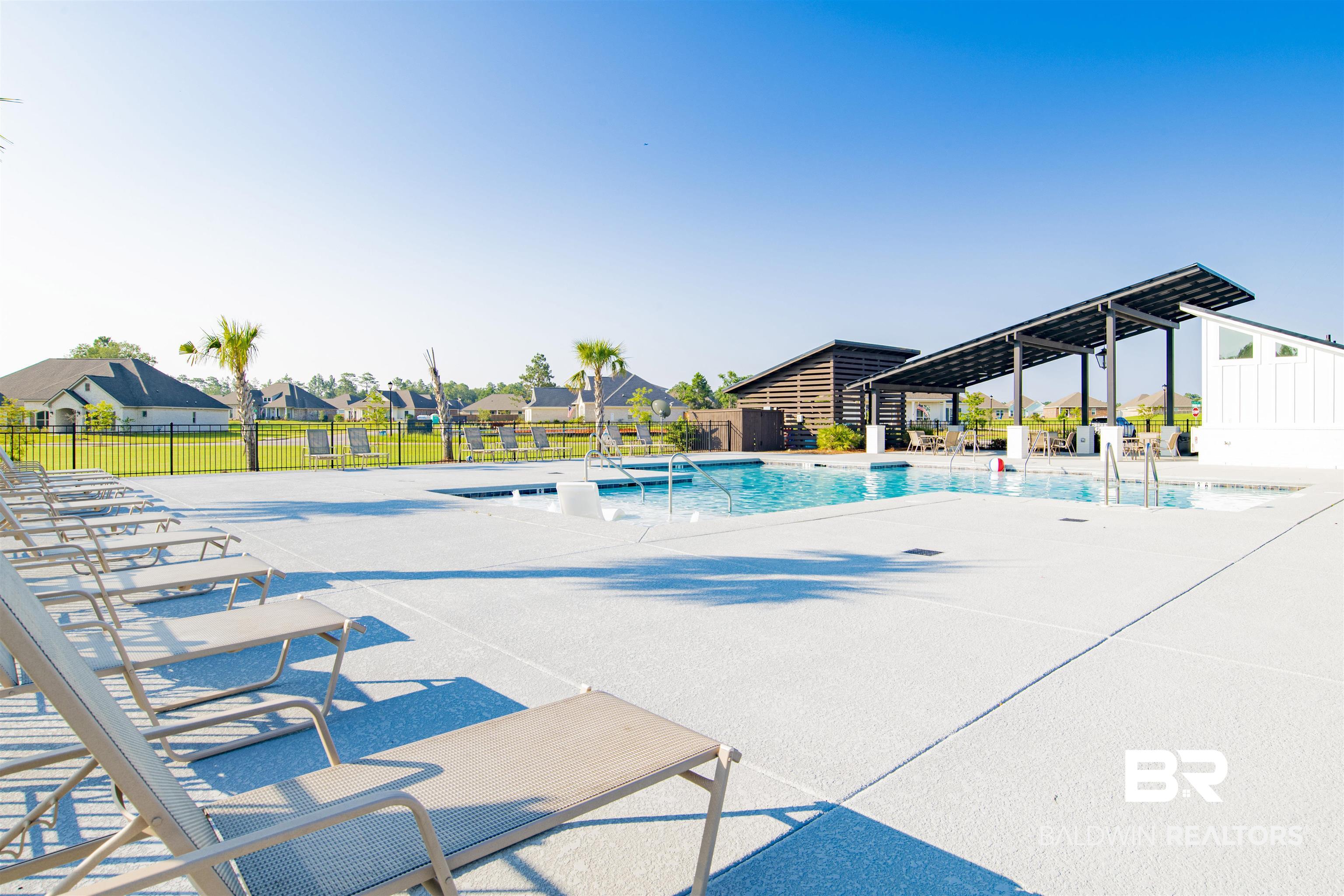8493 Bronze Lane Foley, AL 36535 - Photo 34 of 38 Community pool area featuring a large swimming pool, a covered pavilion with seating, and a separate building with vertical white siding and horizontal wooden accents