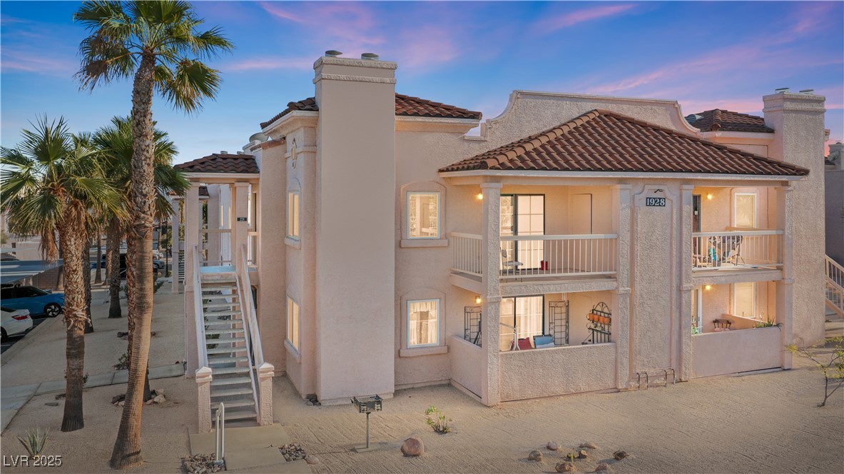 Front of property at dusk with a balcony, stairway, stucco siding, a tiled roof, and a chimney