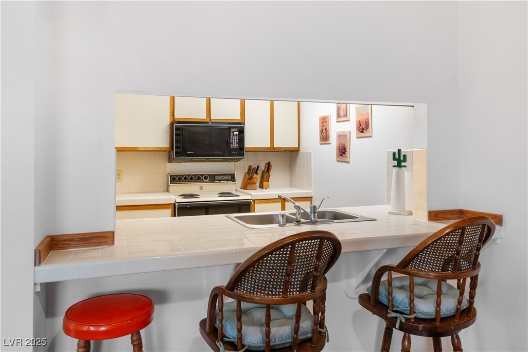 1928 Las Palmas Lane, Unit 228 Laughlin, NV 89029 - Photo 13 of 77 Kitchen featuring black microwave, white electric stove, a sink, and tile countertops