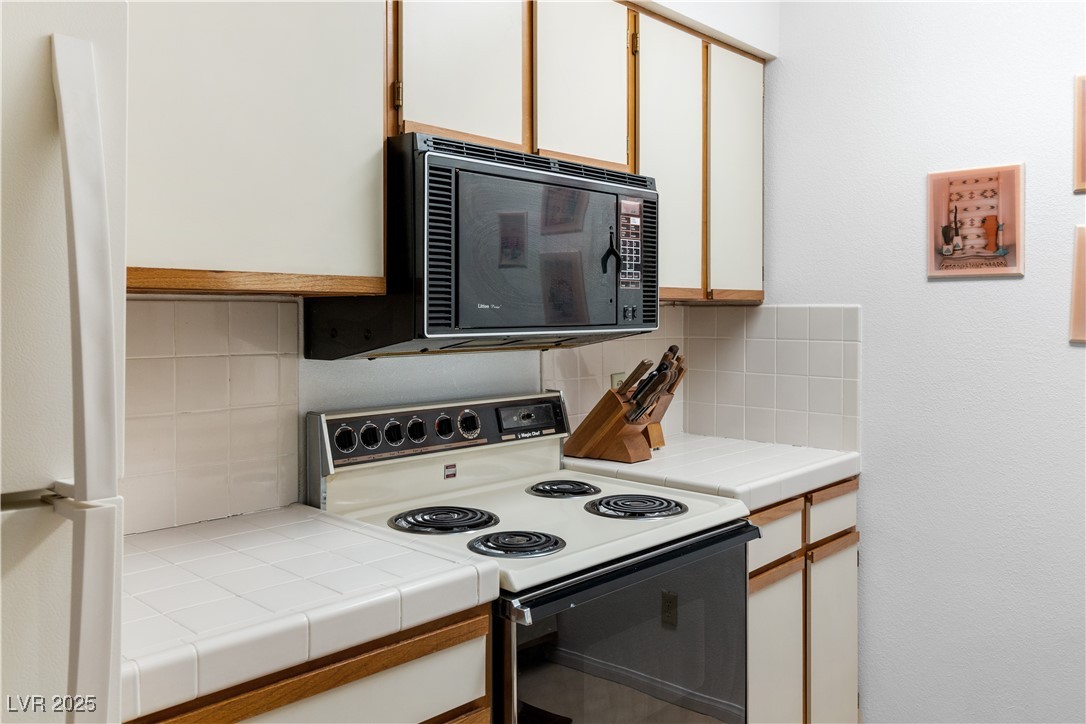 1928 Las Palmas Lane, Unit 228 Laughlin, NV 89029 - Photo 15 of 77 Kitchen featuring electric stove, black microwave, freestanding refrigerator, decorative backsplash, and tile counters