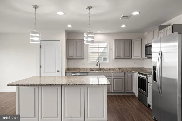 a kitchen with stainless steel appliances granite countertop a sink a stove a refrigerator and island with wooden floor