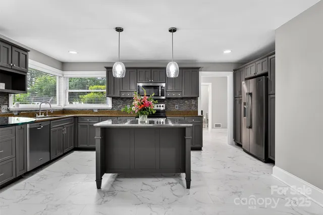 a kitchen with stainless steel appliances granite countertop a refrigerator a sink dishwasher a stove and a dining table with wooden floor