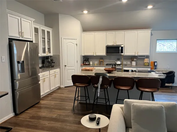 a kitchen with stainless steel appliances granite countertop a refrigerator a stove a sink dishwasher a dining table and chairs with wooden floor