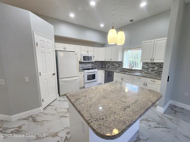 a kitchen with granite countertop white cabinets and white appliances