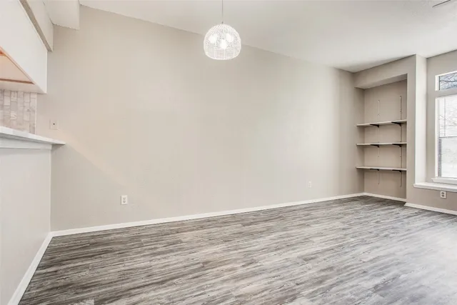 an empty room with wooden floor fireplace cabinet and windows