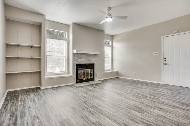 an empty room with wooden floor fireplace cabinet and windows