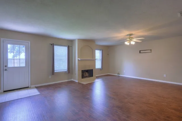 an empty room with wooden floor fireplace and window