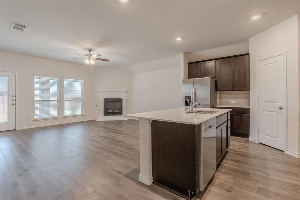 2902 Trusting Way Aubrey, TX 76227 - Photo 7 of 38 Open-concept living area featuring wood-finish flooring, a decorative fireplace with a white mantel, and a ceiling fan
