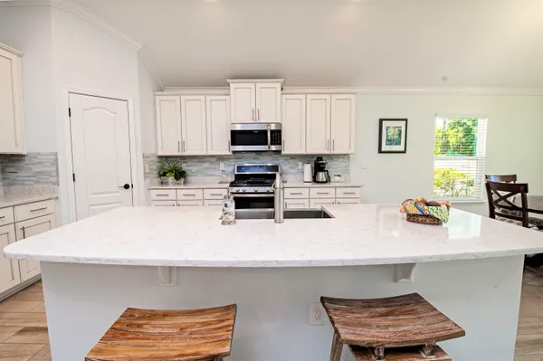 a kitchen with stainless steel appliances a sink a stove a refrigerator white cabinets and wooden floor
