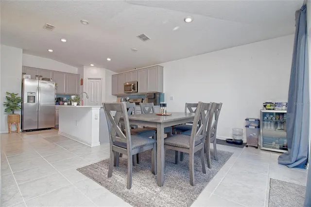 a dining area with stainless steel appliances kitchen island granite countertop a dining table chairs and a refrigerator