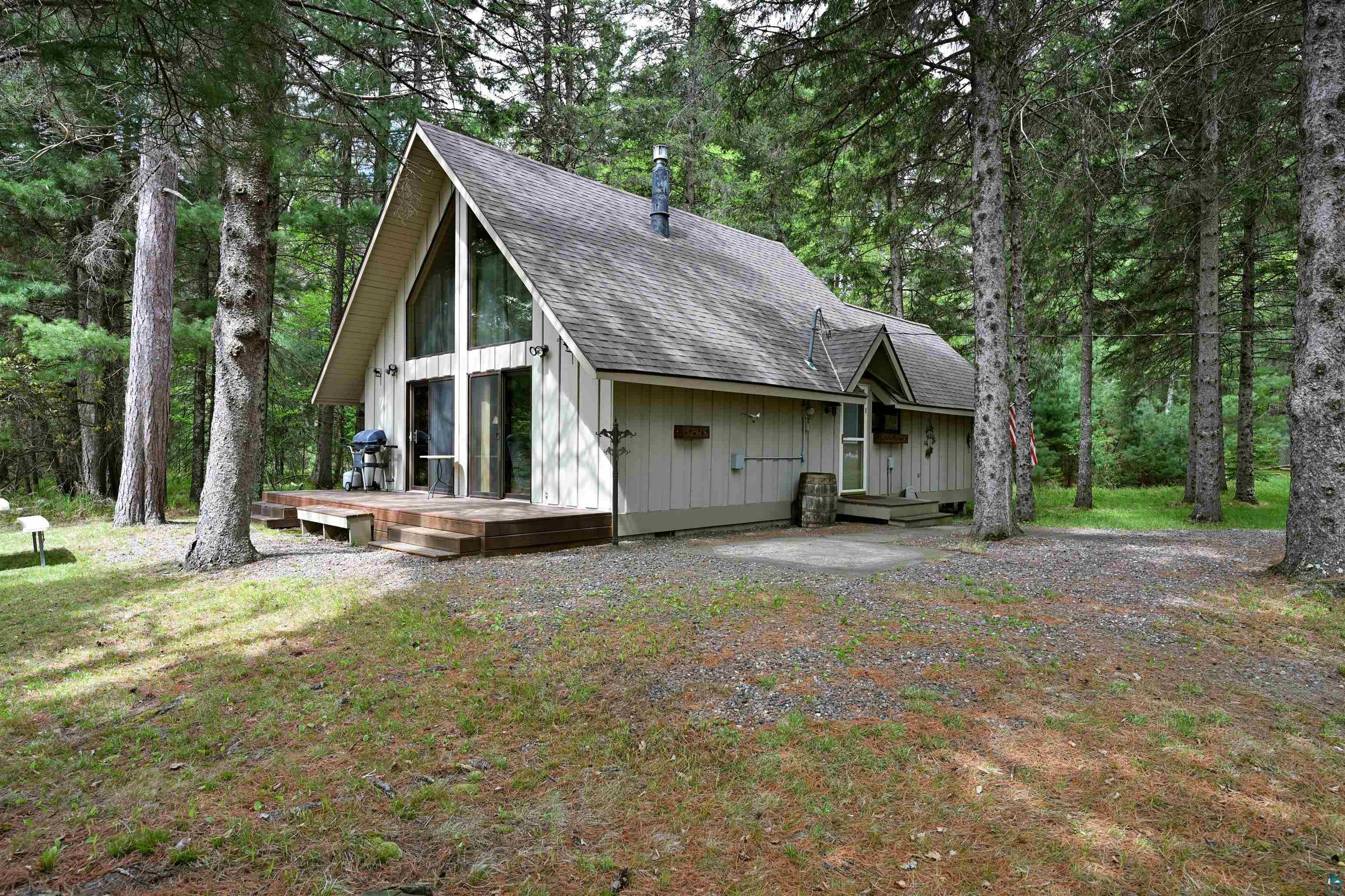 View of front of property with a shingled roof, a wooden deck, and view of wooded area