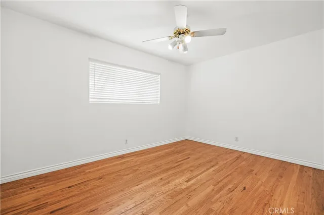 an empty room with wooden floor chandelier fan and windows