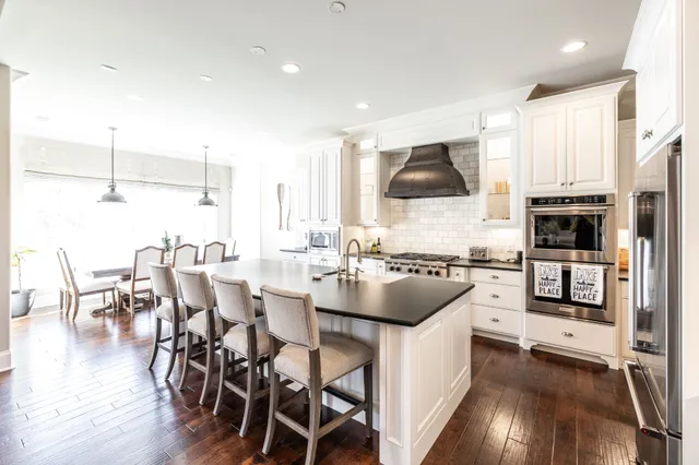 a kitchen with stainless steel appliances a stove a sink a microwave a dining table and chairs with wooden floor