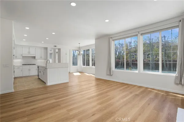 a view of an empty room with wooden floor and a kitchen