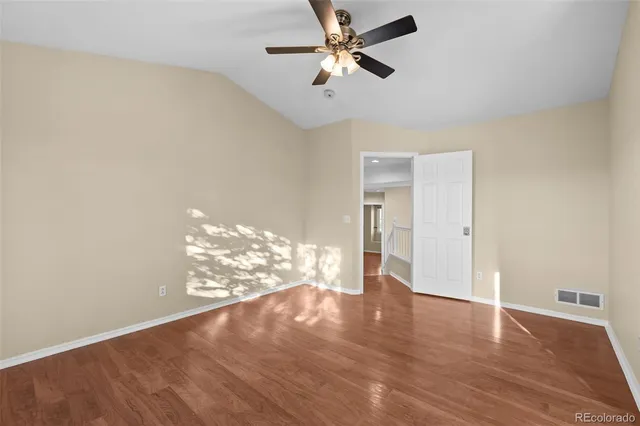a view of an empty room with wooden floor and a ceiling fan