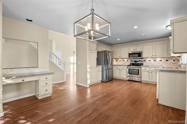a kitchen with stainless steel appliances a stove a sink dishwasher a refrigerator and white cabinets with wooden floor