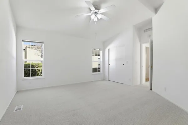 an empty room with chandelier fan and windows