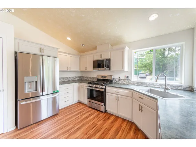 a kitchen with stainless steel appliances granite countertop a refrigerator a sink dishwasher a stove and white countertops with wooden floor