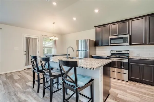 a kitchen with stainless steel appliances kitchen island granite countertop a stove a sink a microwave a dining table and chairs with wooden floor