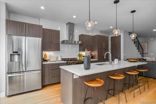 a kitchen with stainless steel appliances granite countertop a sink a stove a refrigerator and chairs with wooden floor