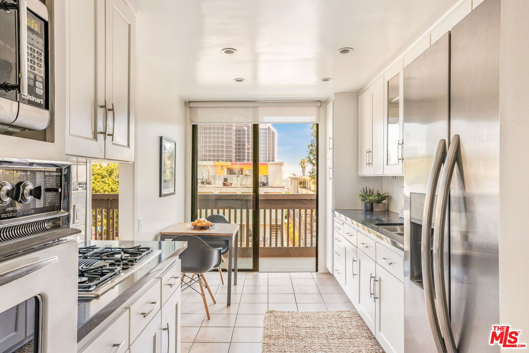 11805 Mayfield Avenue, Unit 202 Los Angeles, CA 90049 - Photo 7 of 17 a open kitchen with stainless steel appliances kitchen island granite countertop a refrigerator a stove a dining table and chairs with wooden floor