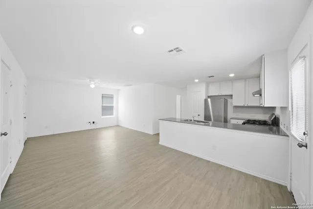 a large white kitchen with a stove a sink a refrigerator and white cabinets with wooden floor