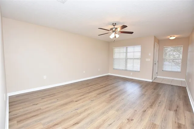 an empty room with wooden floor ceiling fan and windows