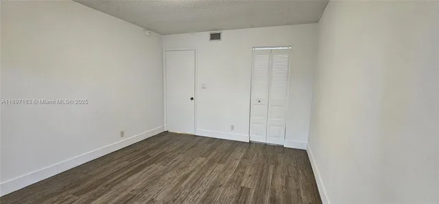 a view of an empty room with wooden floor and closet