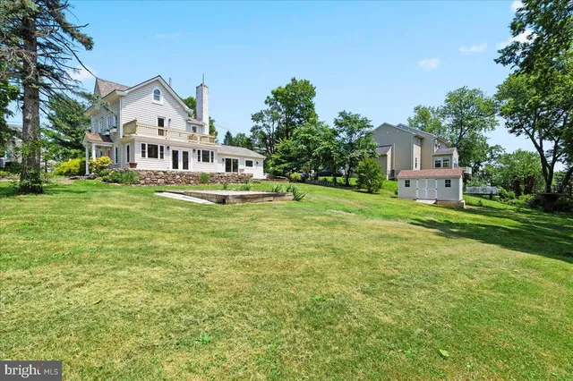 a white house that has a big yard and a big trees with wooden fence