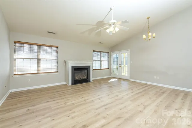 an empty room with wooden floor chandelier and windows