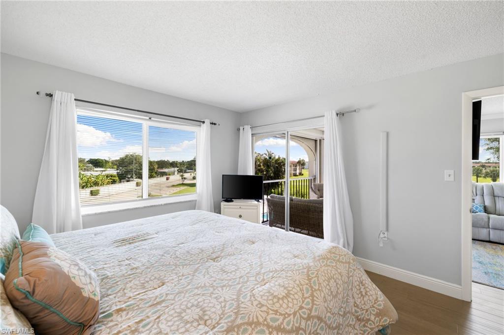 5 High Point Circle West, Unit 307 Naples, FL 34103 - Photo 17 of 31 Bedroom with access to exterior, dark wood-style floors, and a textured ceiling
