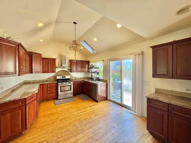 a large kitchen with stainless steel appliances wooden cabinets a stove a sink and a wooden floors